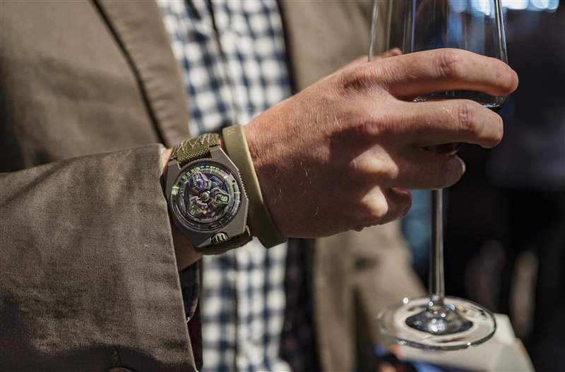 一位拿著香檳酒杯的男士手腕上的 Urwerk 手表。